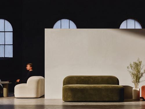 A modern office or lounge area with two rounded, plush sofas, arched windows, and a man sitting in motion-blur in the background.