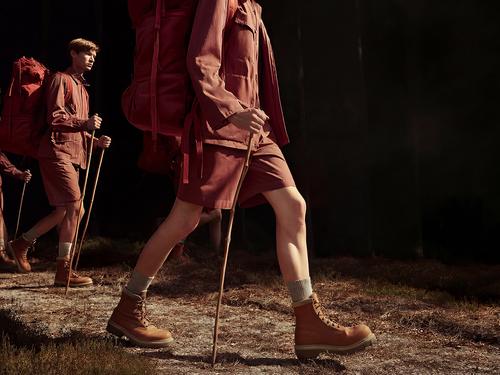 Three people in matching shirts, shorts, and hiking boots walking on a path in a forest with red backpacks and hiking sticks.