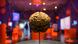 A large model of a brain is mounted on a stick with red display boxes visible in the distance behind it. A large model of a brain is mounted on a stick with red display boxes visible in the distance behind it.