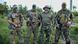 A group of four men wearing military fatigues, standing with weapons in a grassy field, looking at the camera A group of four men wearing military fatigues, standing with weapons in a grassy field, looking at the camera