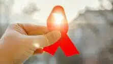 A hand holds a red ribbon symbolizing AIDS support and awareness.