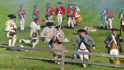 Revolutionary War reenactment on field with soldiers from both sides.